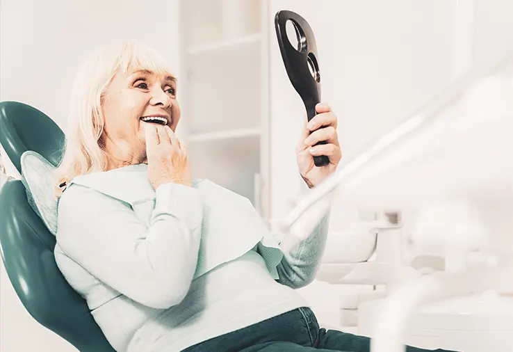Une femme âgée se regarde dans le miroir après avoir mis sa prothèse dentaire